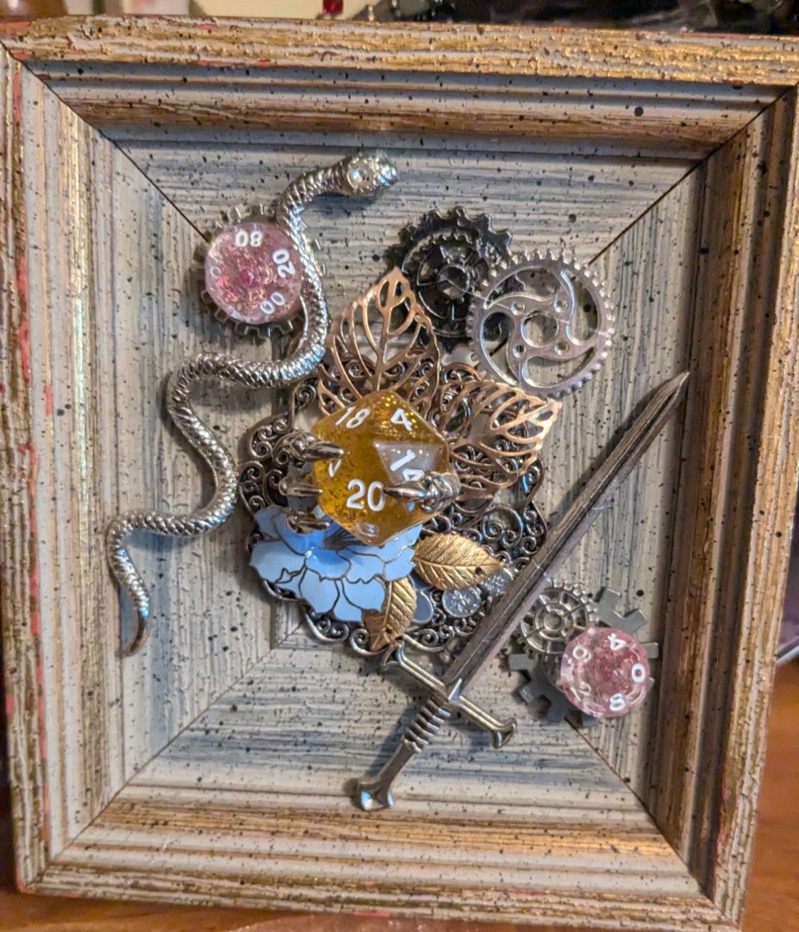 Framed assemblage — D20, snake, sword, gears and filigree leaves