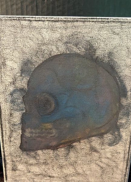 A blue-grey skull in profile emerging from a smoky charcoal ground