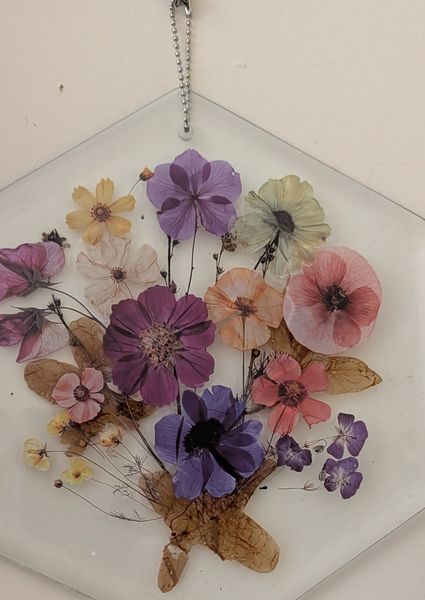 Purple pink and cream pressed blooms with seed pods on a hexagonal glass panel